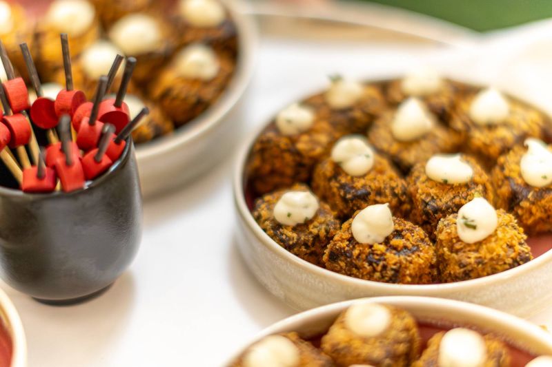 Close-up of plated canapés in bowls topped with a light sauce, with decorative cocktail sticks in a nearby container on a table.