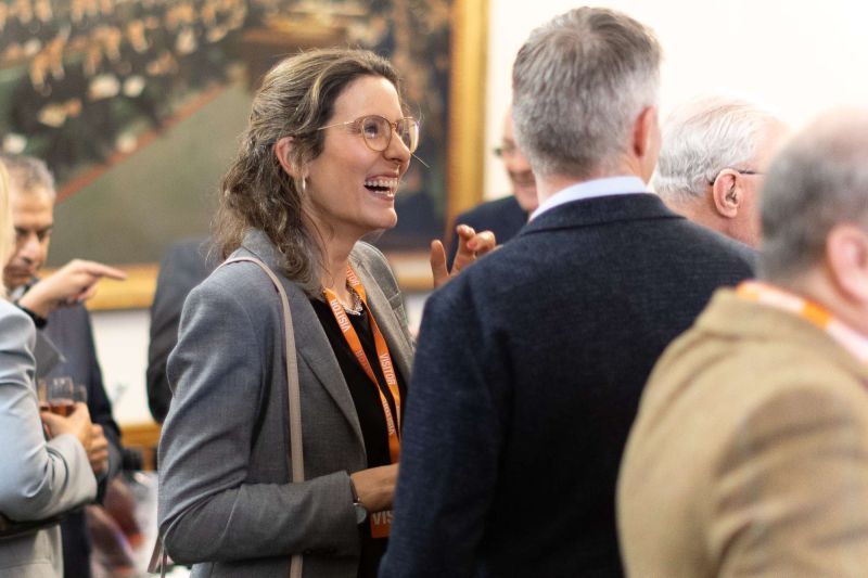 Group of attendees gathered closely in conversation; one person holds a drink while others face inward in a crowded networking setting.