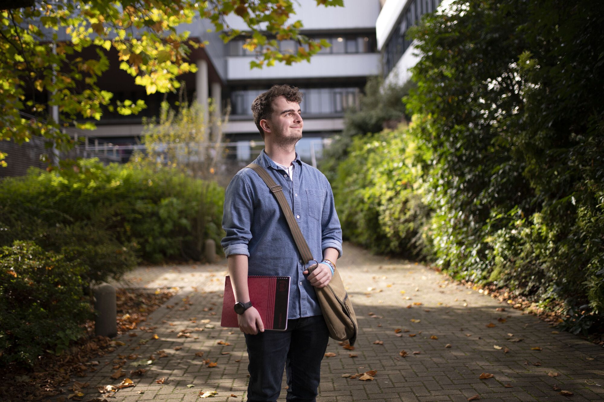 Male PhD Researcher standing under the trees at Coleraine campus, holding a folder