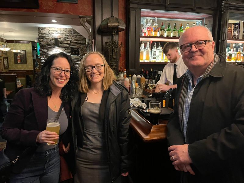 two females and one male in a bar posing with drinks