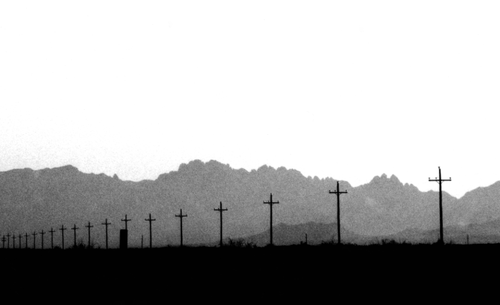 A desert landscape with mountains in the distance and a long line of telegraph poles receding into the distance. 