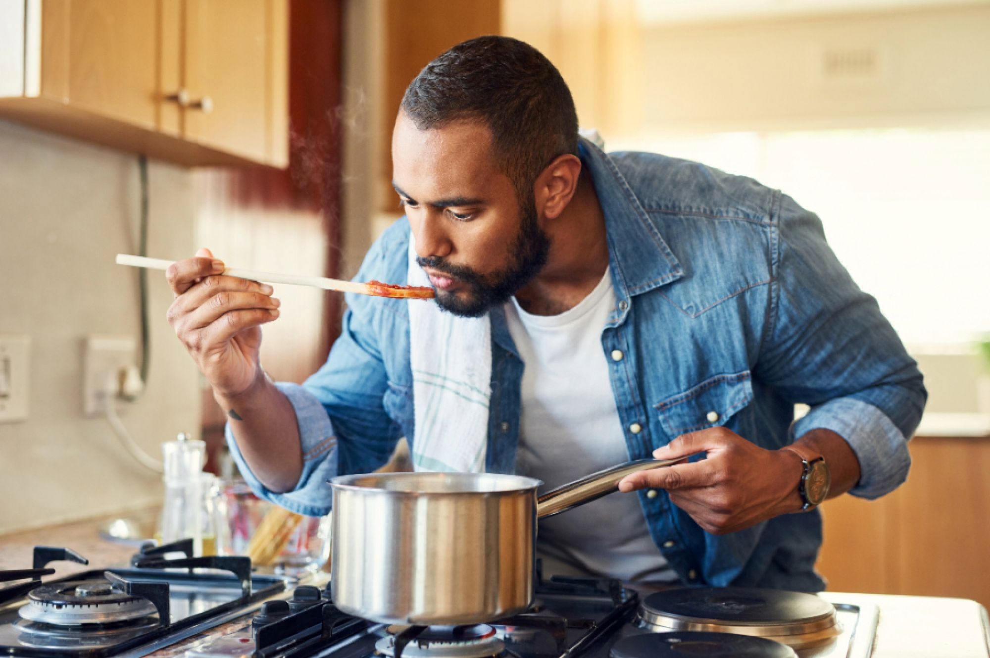 Man tasting food cooking on a pot with a wooden spoon