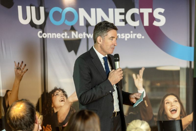 Panel host Jim Fitzpatrick speaking into a microphone in front of UU Connects sign.