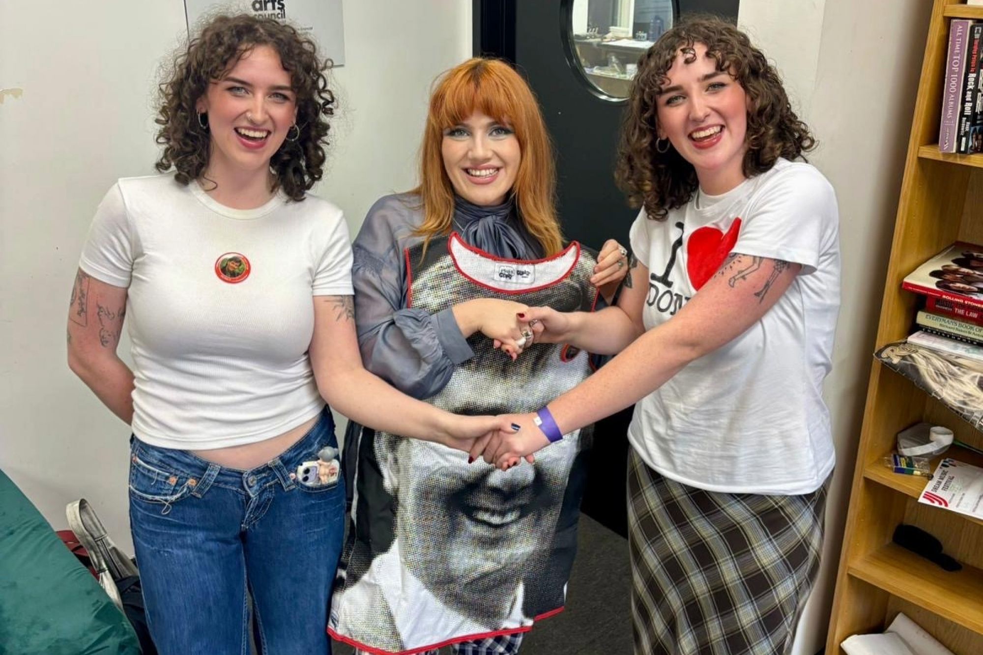 three women holding hands and one holding a graphic print dress with a man's face