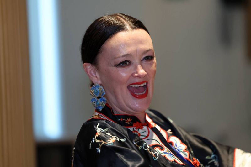 Close-up of a person at an indoor venue wearing patterned clothing and large statement earrings, seated and turned slightly to the side.