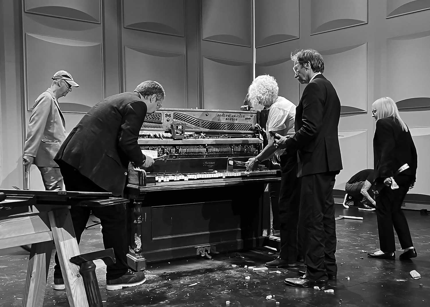  a black and white photograph of a recreation of a famous fluxus performance, people surrounding a piano