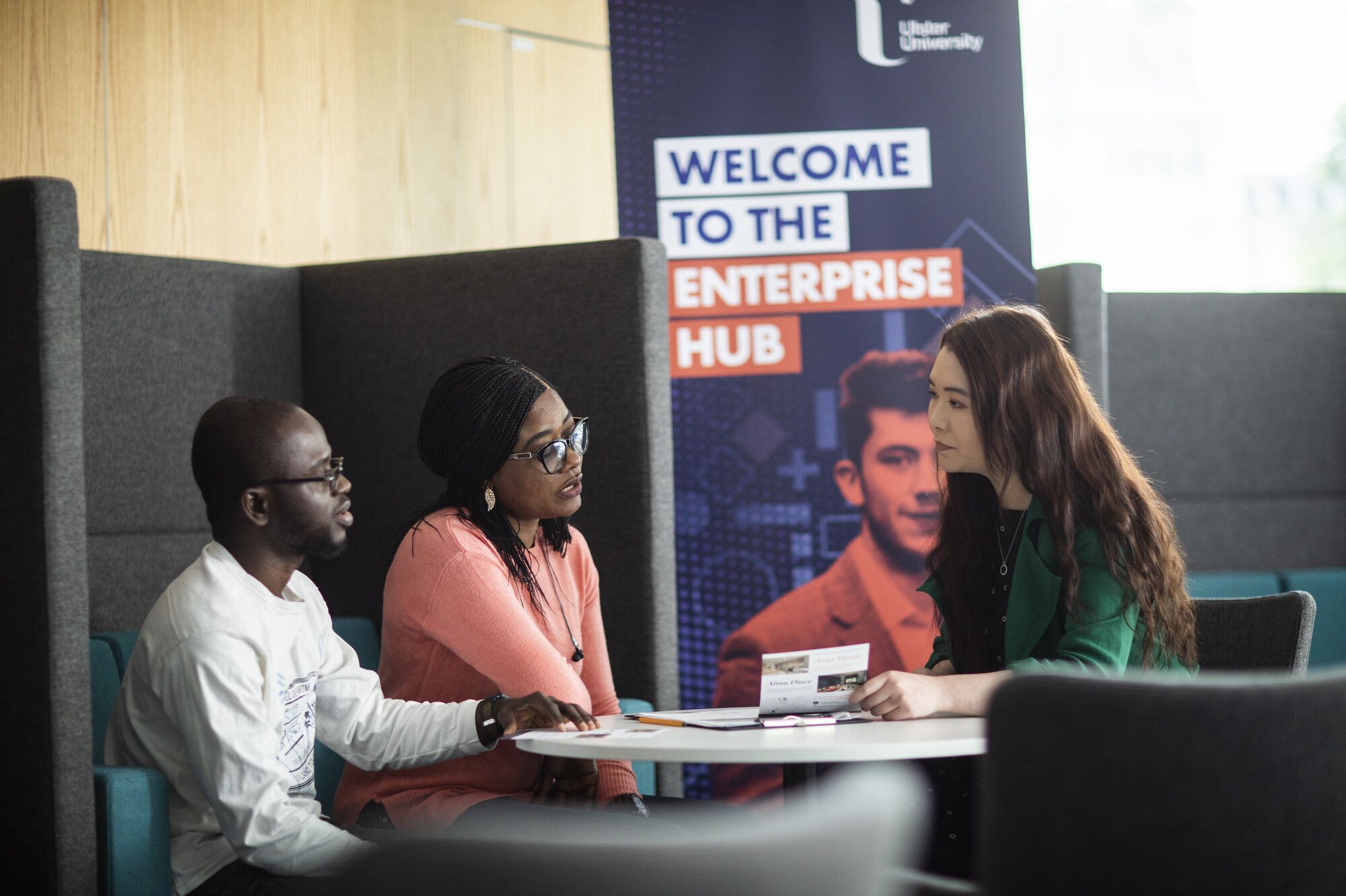Three students sitting down and talking next to an Enterprise Hub pull-up stand