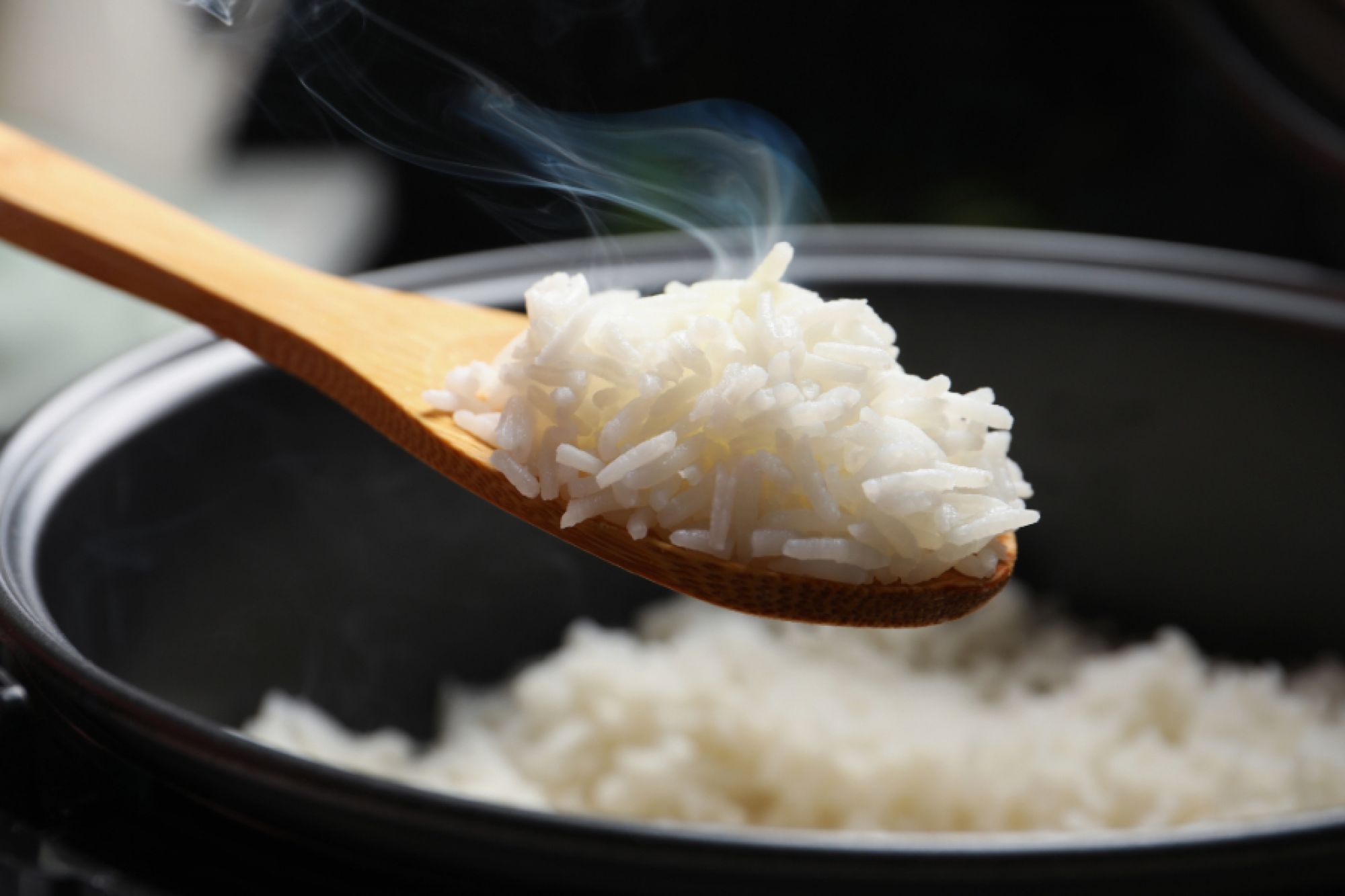 A wooden spoon taking up some rice cooking in a pot